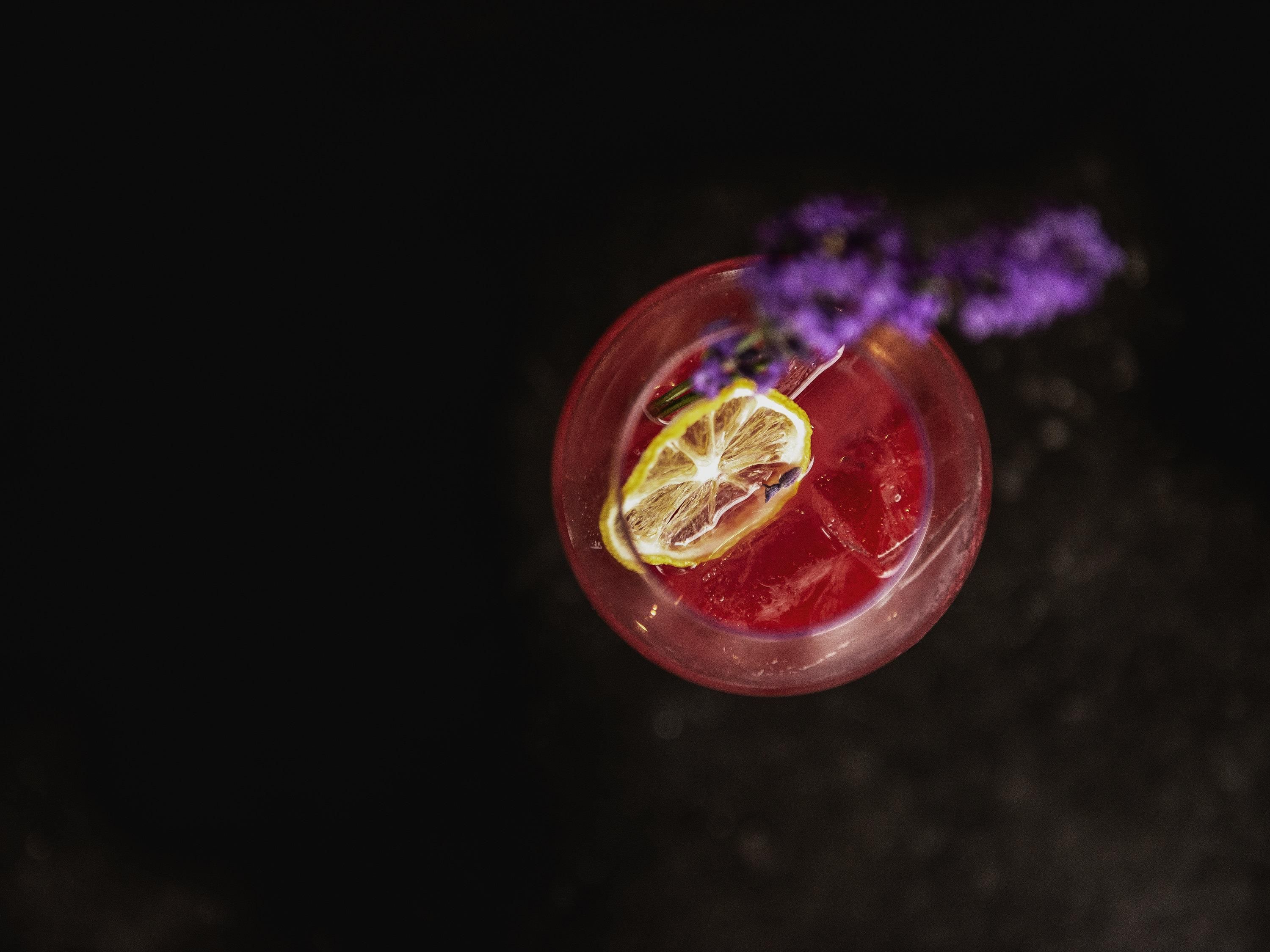 A cocktail with a slice of lemon and a purple flower garnish.