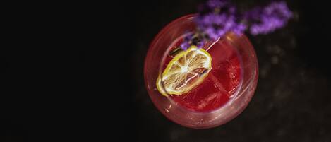 A cocktail with a slice of lemon and a purple flower garnish.