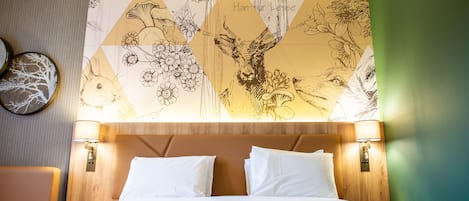 Hotelkamer met een bed, twee bedlampen, een hoofdeinde en een muur met een geometrisch bloemenpatroon.