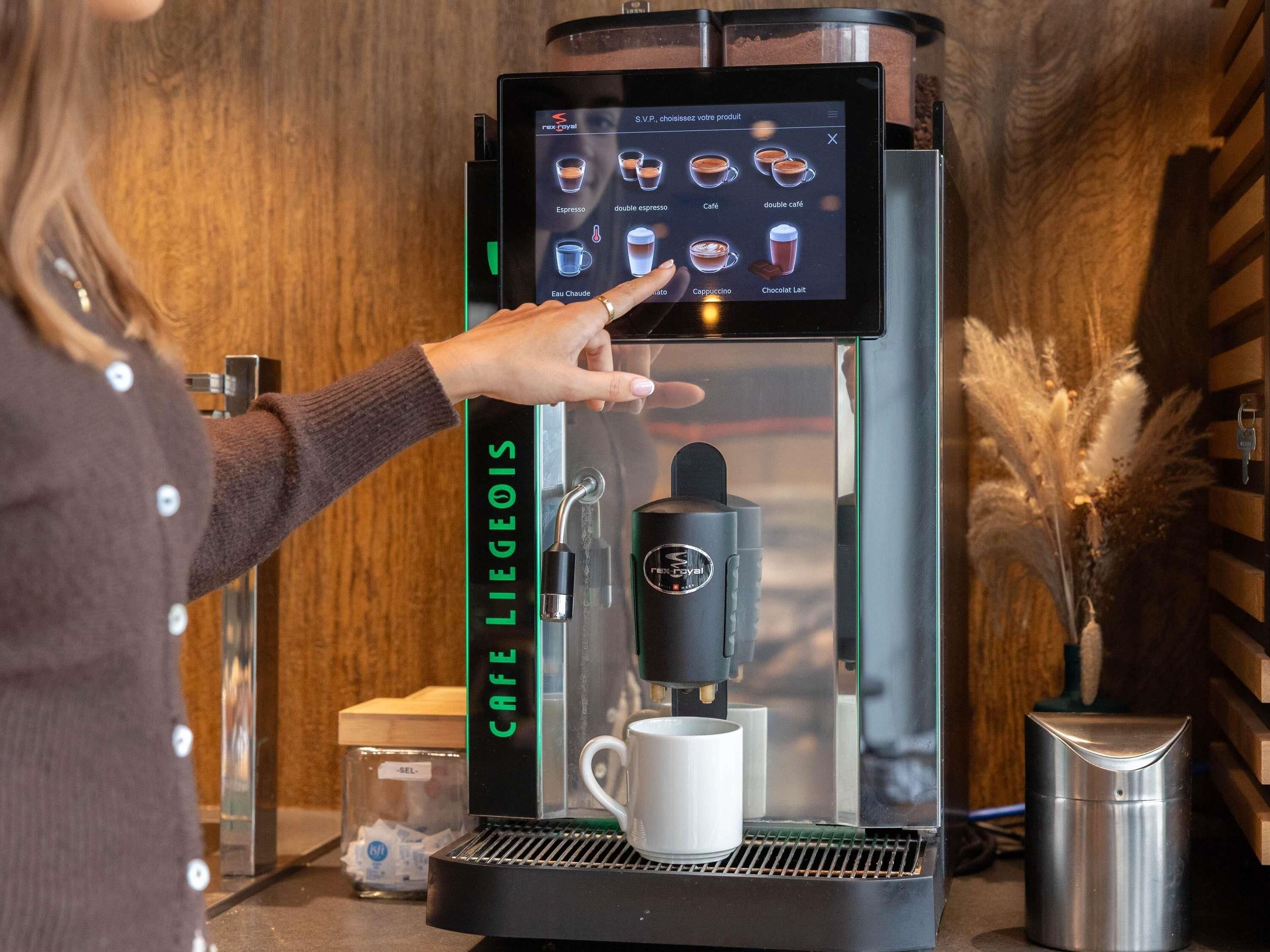 Una persona usando una máquina de café, eligiendo una bebida en una pantalla táctil.