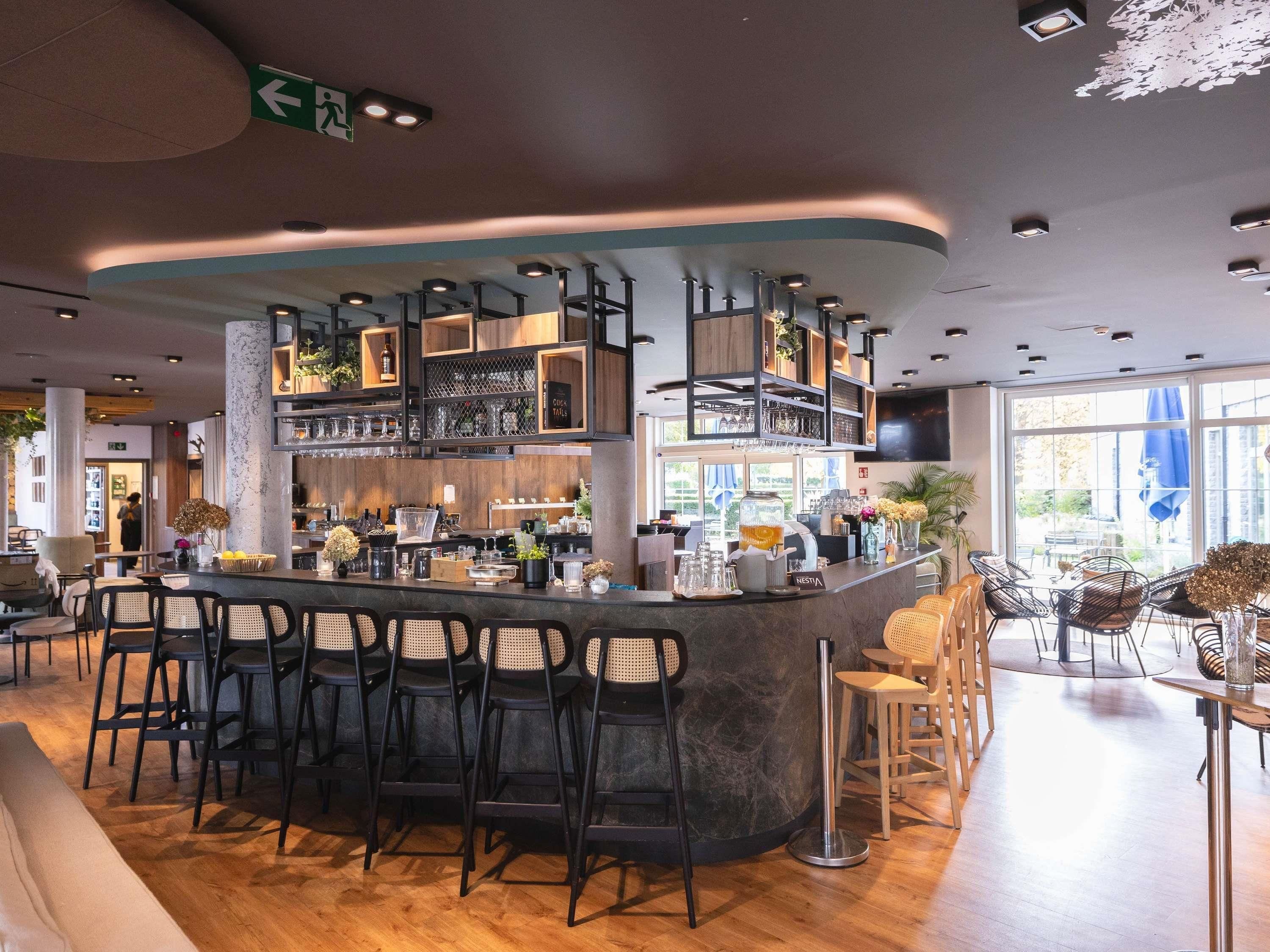 Een moderne bar met een gebogen toonbank, meerdere krukken en diverse barbenodigdheden en glaswerk.