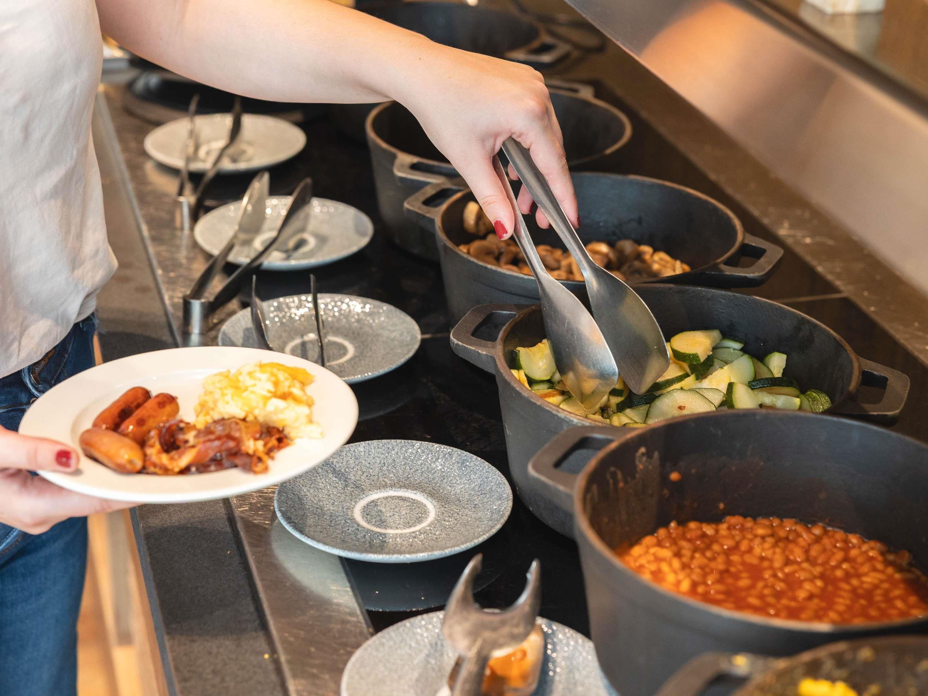 A person serving food from a pot, with plates of food and utensils visible.