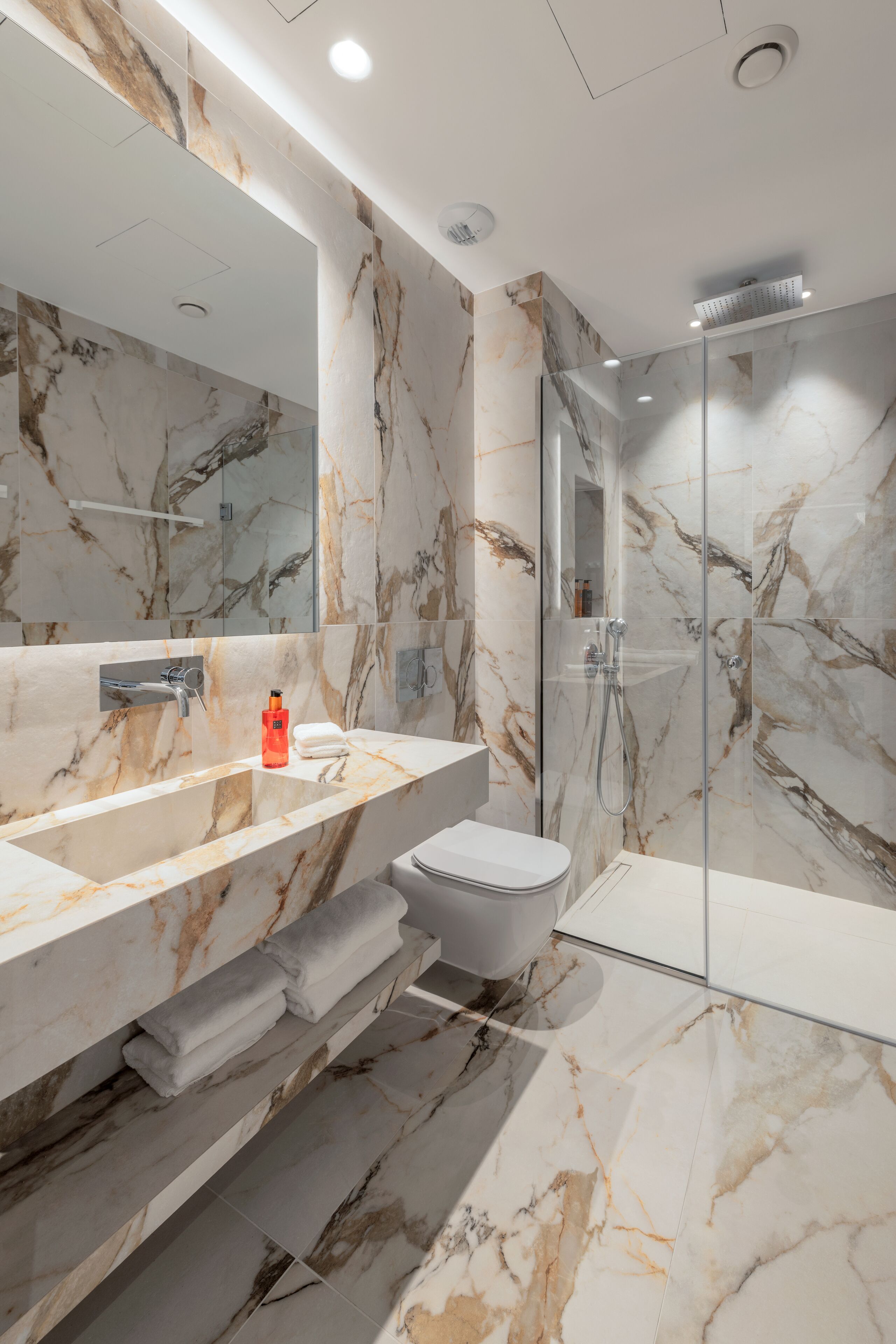A modern bathroom with a marble vanity, a glass shower enclosure, and a toilet.