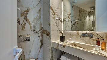 Un baño moderno con paredes de mármol, un espejo grande y un mueble de tocador con artículos de aseo.