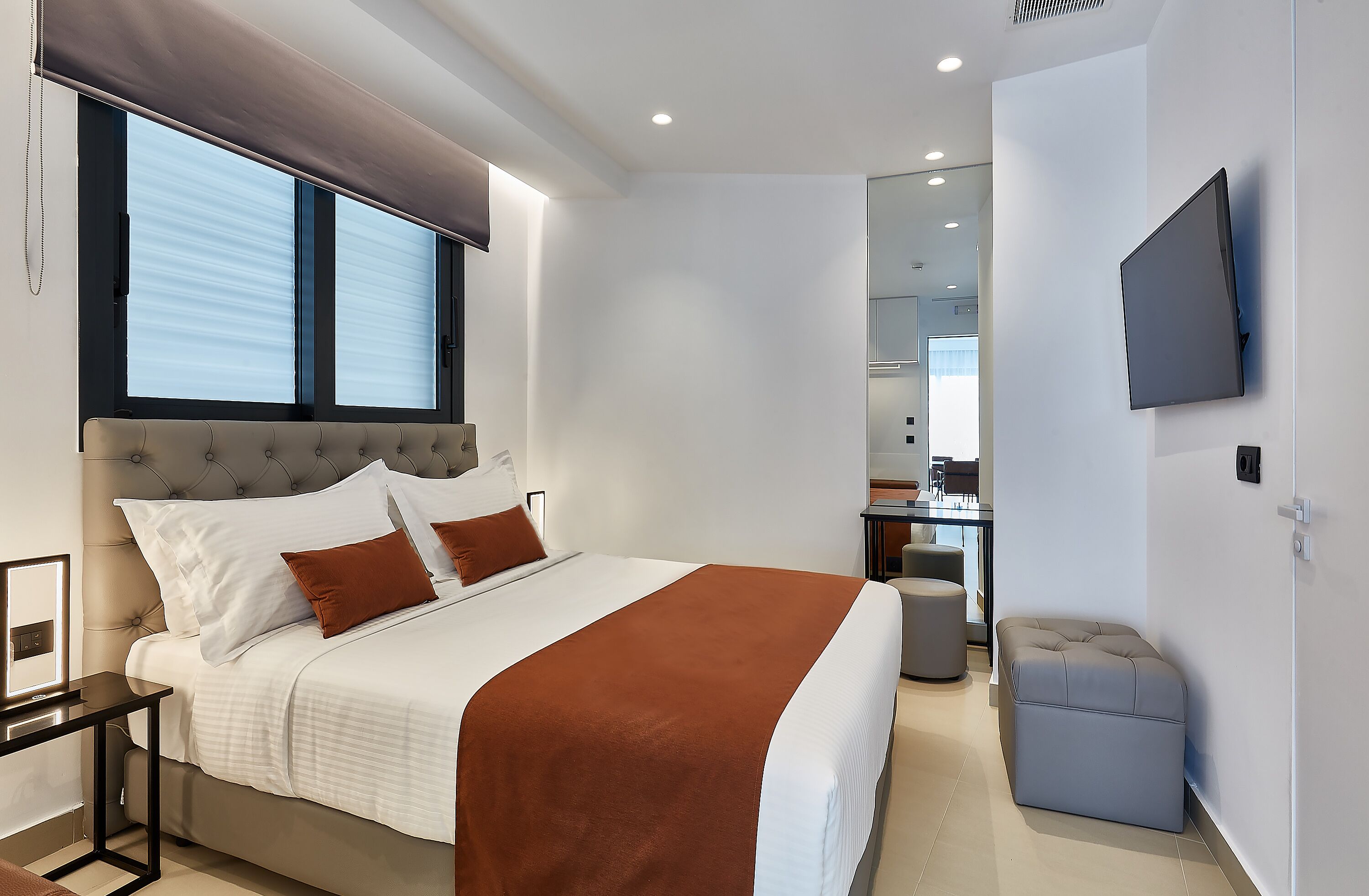 Una habitación de hotel moderna con una cama grande, una mesita de noche, un televisor de pantalla plana en la pared y un pequeño rincón de descanso.