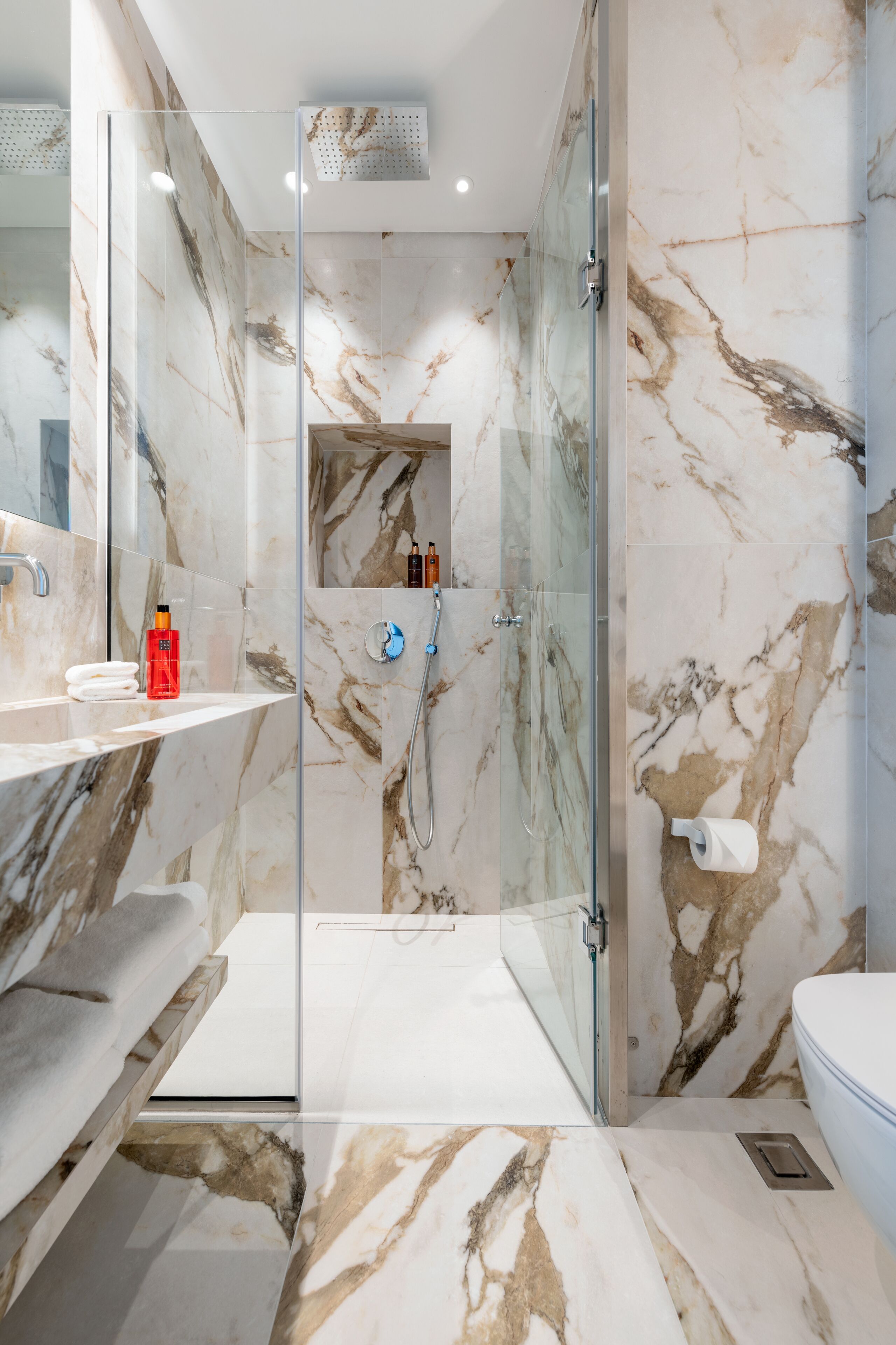 A modern bathroom with a glass-enclosed shower, marble walls, and a white sink with a towel rack.