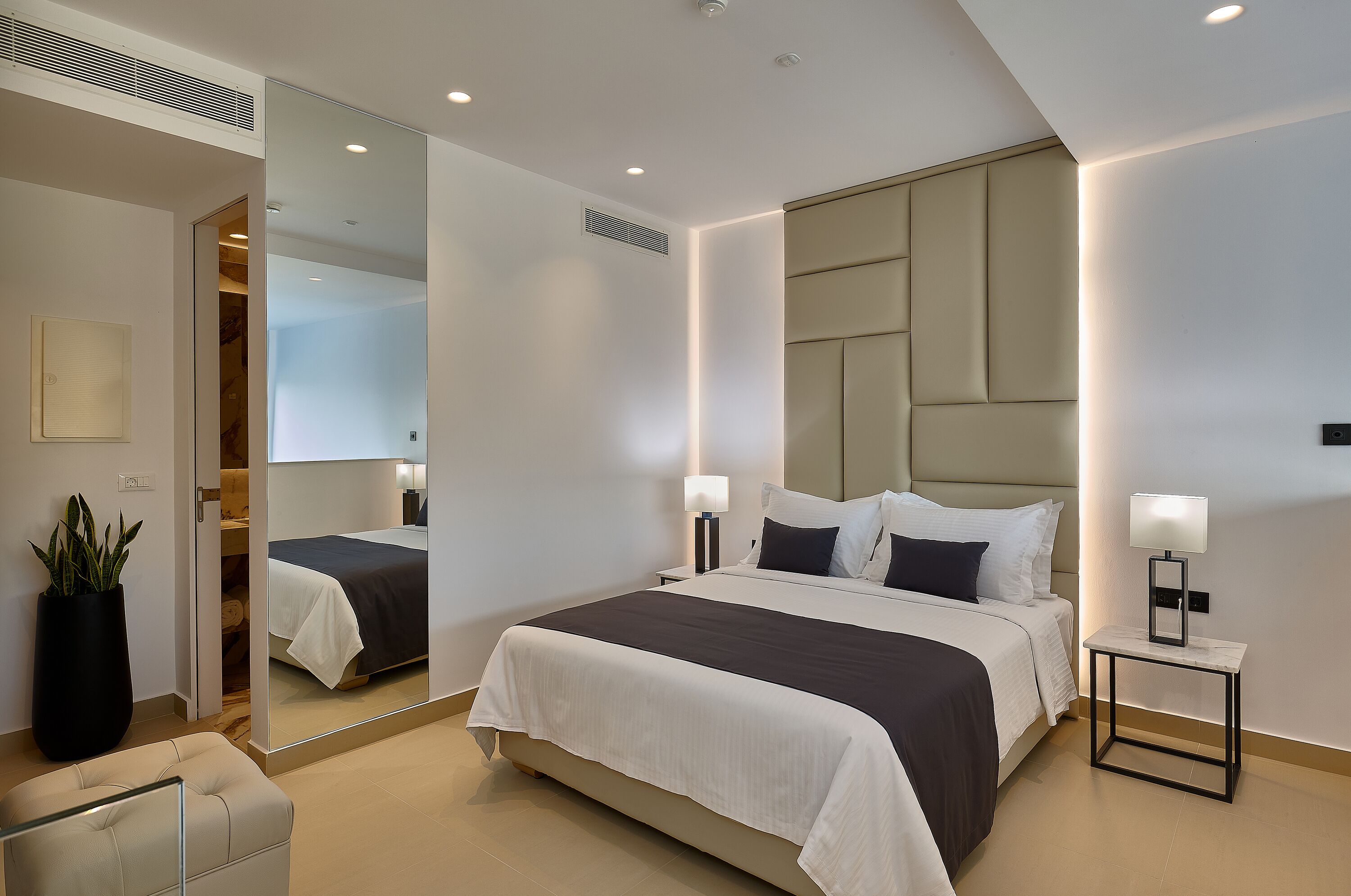 Une chambre d’hôtel moderne avec un grand lit, des tables de chevet, un miroir et une plante en pot.