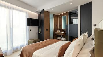 A modern hotel room with a large bed, a TV mounted on the wall, a wardrobe, and a bathroom visible through a glass door.