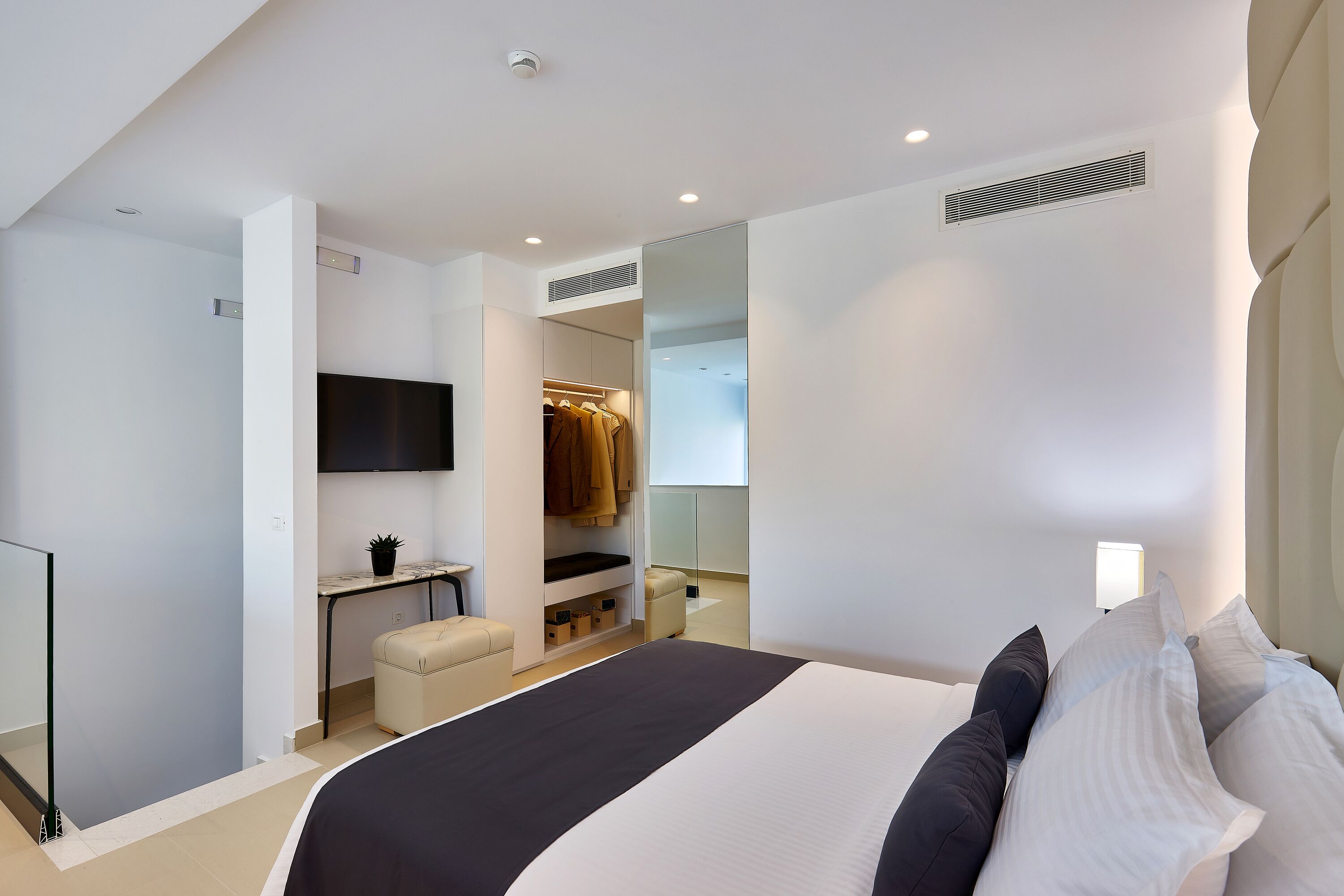 Ein modernes Schlafzimmer mit einem großen Bett, einem begehbaren Kleiderschrank, einem Wand-Fernseher und einer Nachttischlampe.