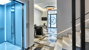 Corredor interno com elevador azul, escada e área de recepção de design moderno.