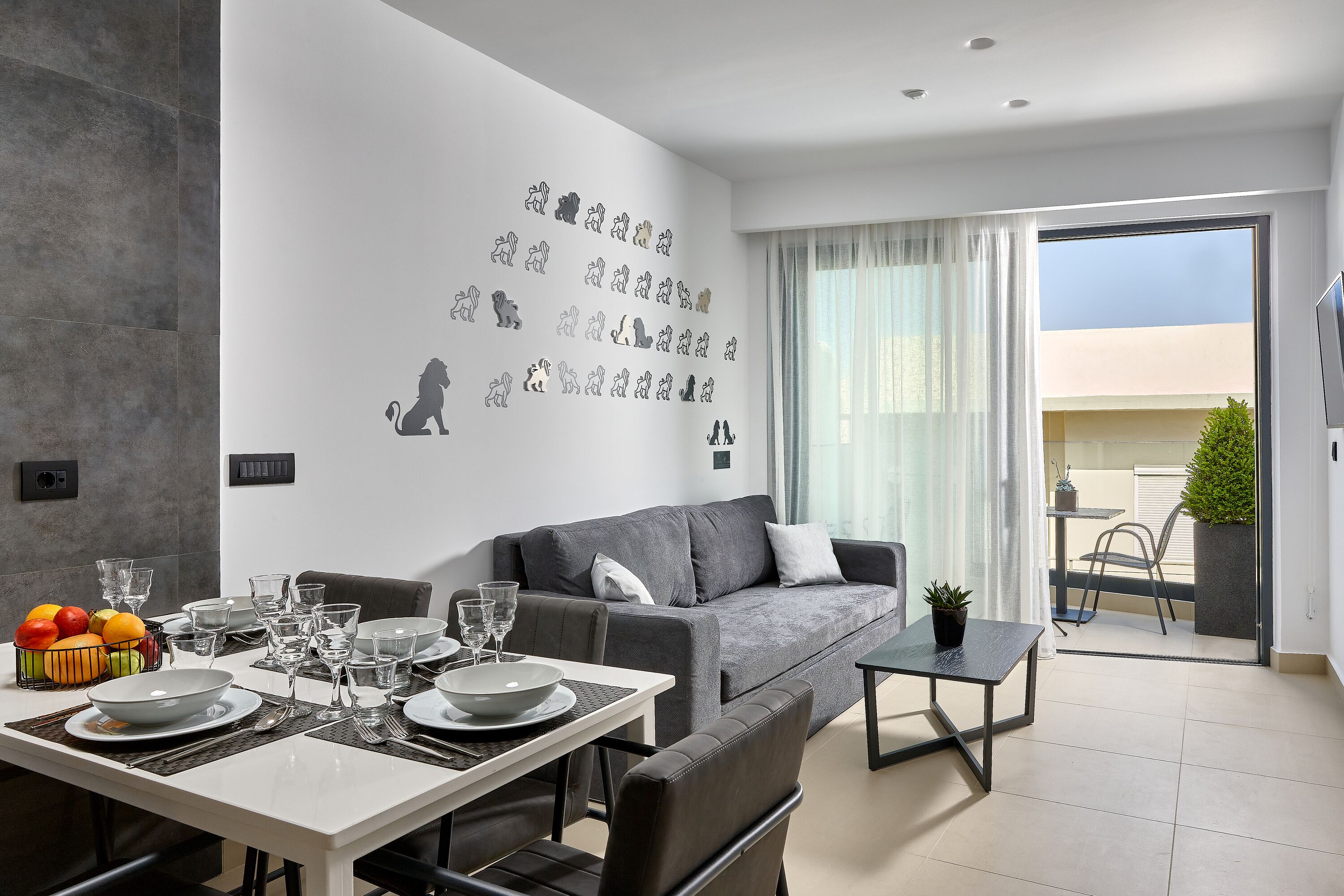 A modern living room with a dining area, grey sofa, and a balcony with a plant.