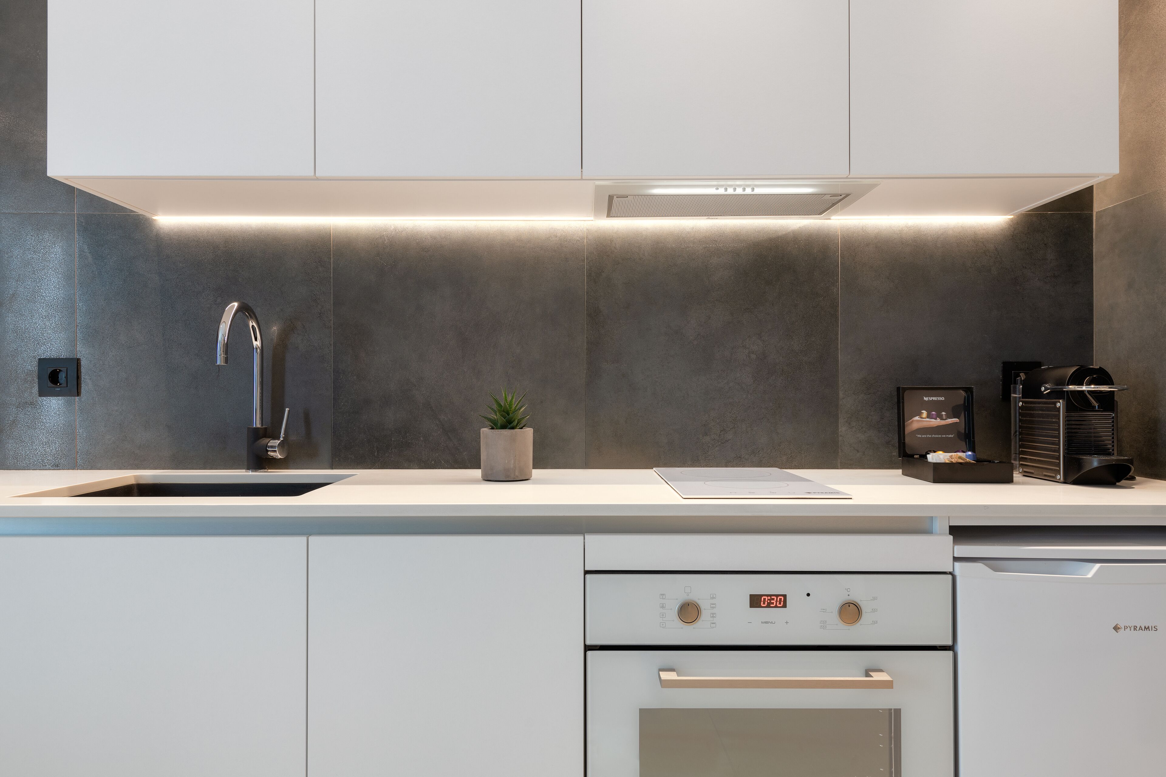 A modern kitchen with a stainless steel sink, a built-in oven, and a coffee machine.
