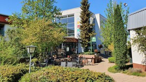 A modern building with a glass facade, outdoor seating area, and a staircase leading to the entrance. - Sport Hotel Kenzingen (Kenzingen)