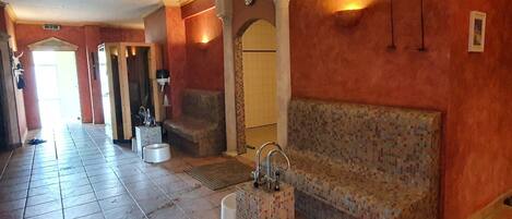 A hotel lobby with a tiled floor, a reception desk, a seating area with a patterned bench, and a wall-mounted clock.