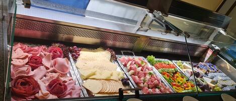 Mostrador de charcutería con diversos tipos de carne, quesos y frutas.