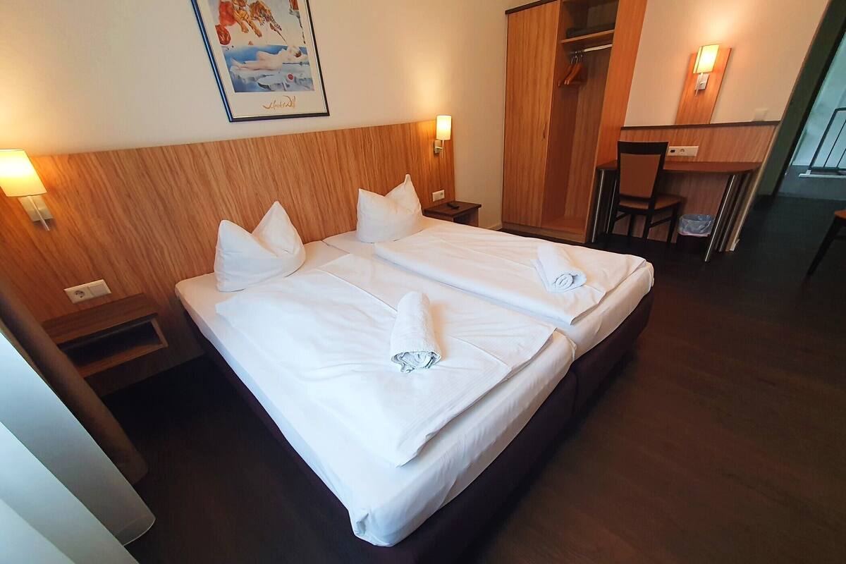 A hotel room with two beds, wooden headboard, bedside lamps, a desk, and a chair.