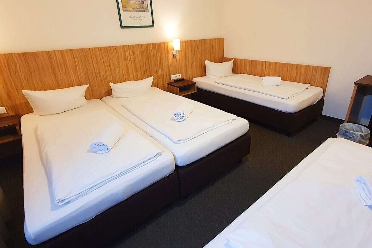 A hotel room with two single beds, a wooden headboard, a nightstand, and a wall-mounted lamp.
