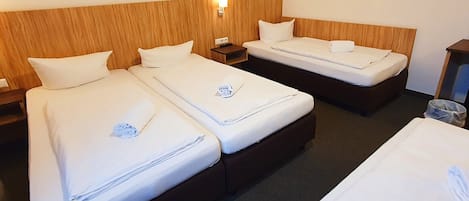 A hotel room with two single beds, a wooden headboard, a nightstand, and a wall-mounted lamp.