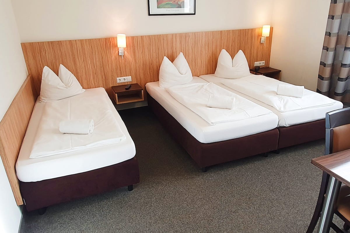 A hotel room with two beds, wooden headboards, bedside tables, and a small desk.