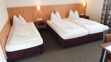 Une chambre d’hôtel avec deux lits, des têtes de lit en bois, des tables de chevet et un petit bureau.