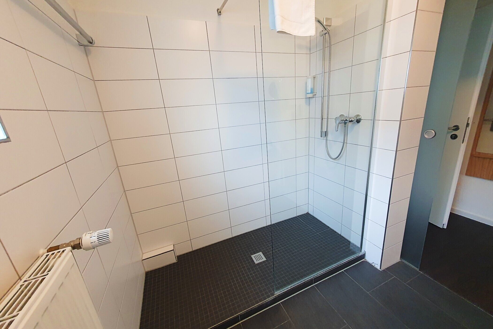 Un espace douche moderne avec des murs recouverts de carreaux blancs et un sol noir.