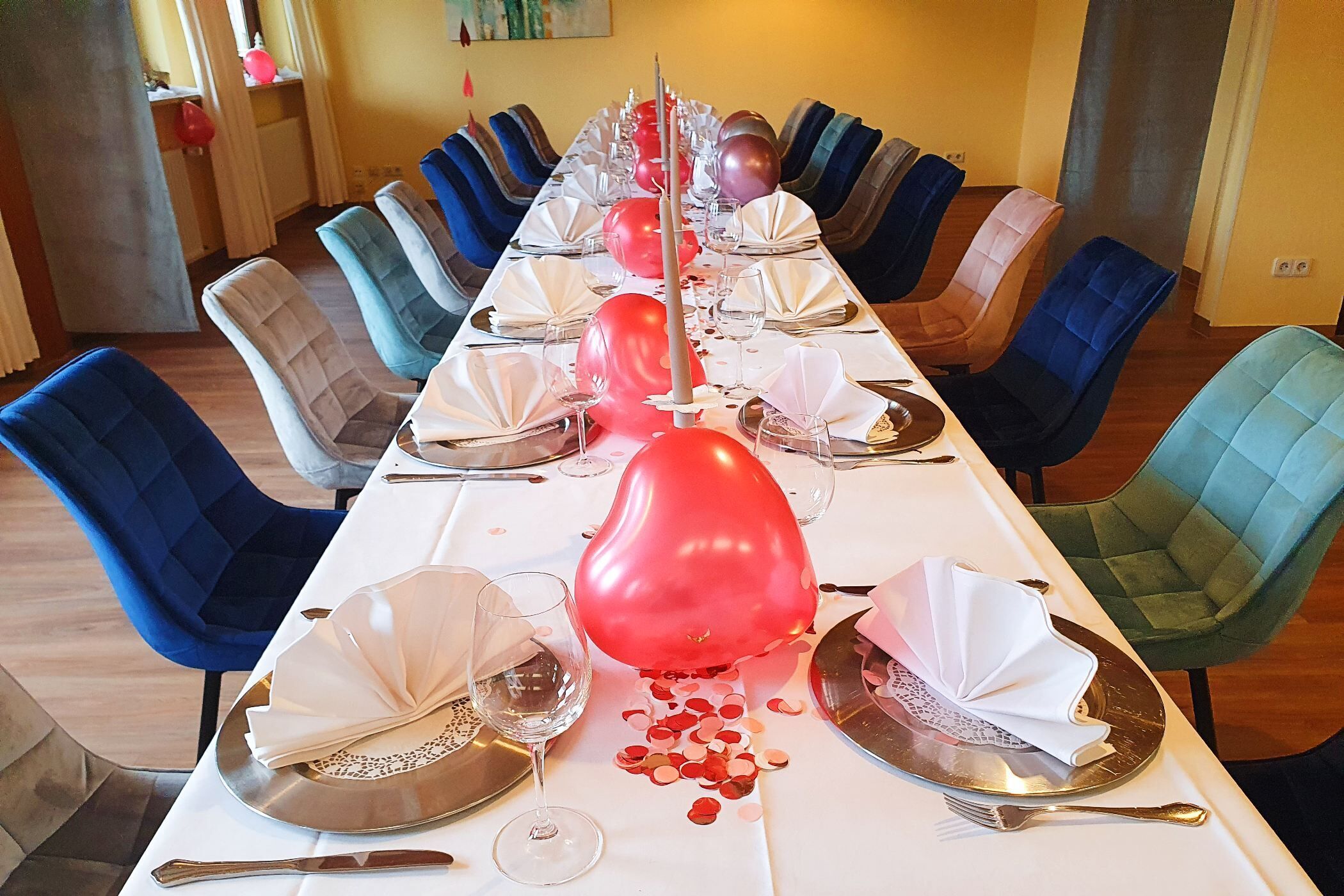 A long dining table set with chairs, plates, cutlery, and balloons.
