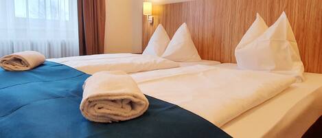 Habitación de hotel con dos camas, cada una con ropa blanca de cama y almohadas, cabeceros de madera y una lámpara fijada a la pared.