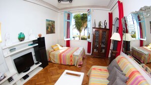 Quarto com duas camas, um sofá, uma televisão e uma janela com cortinas vermelhas.