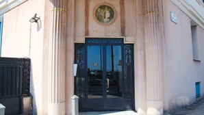 Entrada de um edifício com uma porta preta, colunas e uma placa com a inscrição "BEL-AVVR".