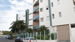 A modern building with a white facade, multiple balconies, and a parking area with several cars. - Sea Front, Front Native Forest (Florianópolis)