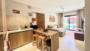 A modern kitchen with a dining area, a sofa, and a view of the outdoors. - Forest View Apartments (Serrekunda)