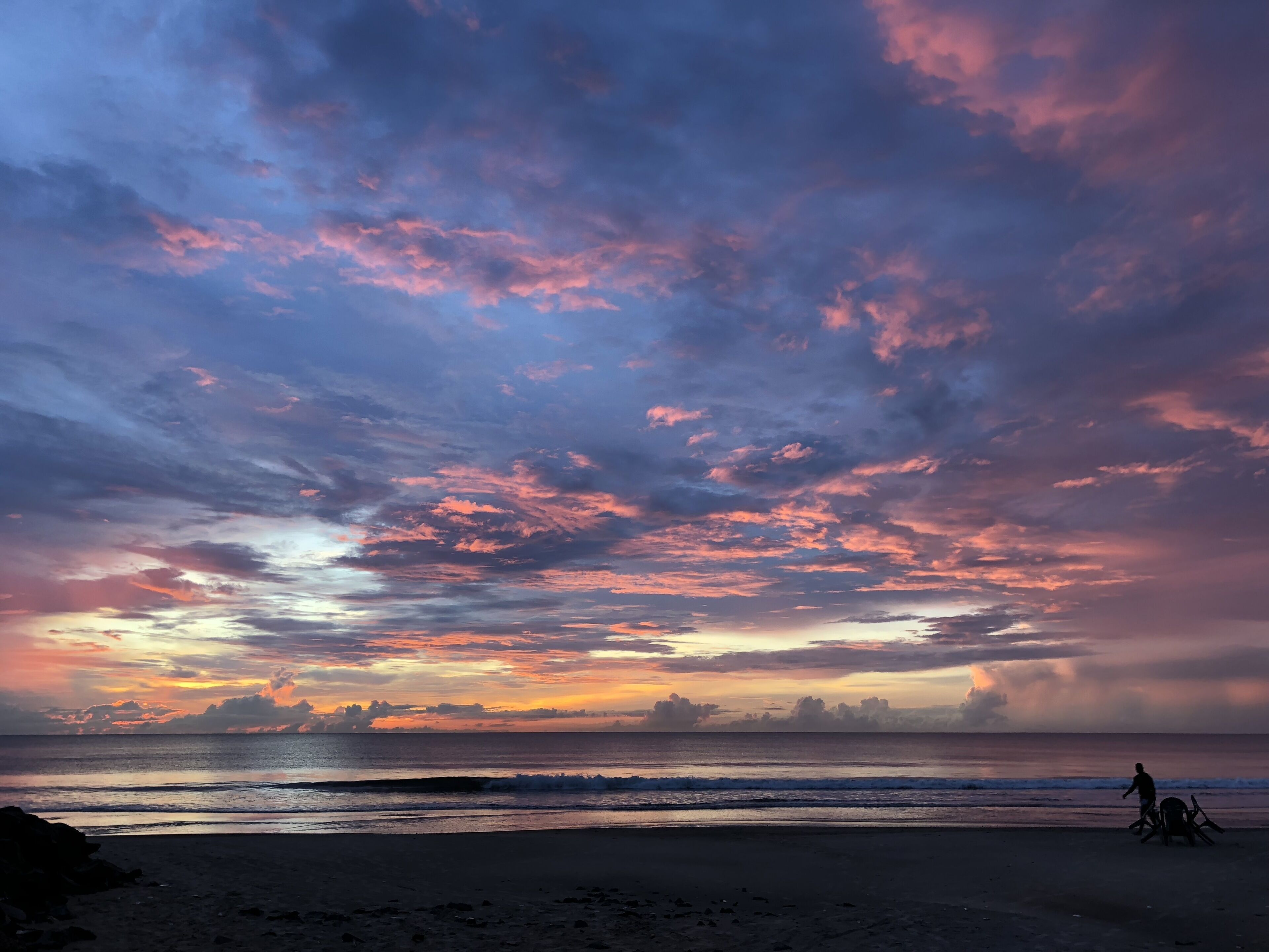 A beach with a sunset and a person on a bicycle.
