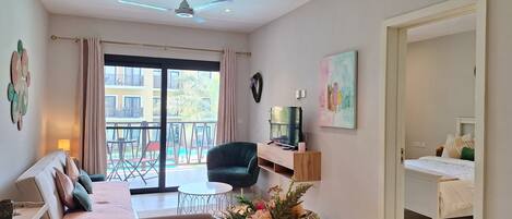 Una sala de estar moderna con un sofá, una mesa de centro, un televisor y un balcón con mobiliario exterior.