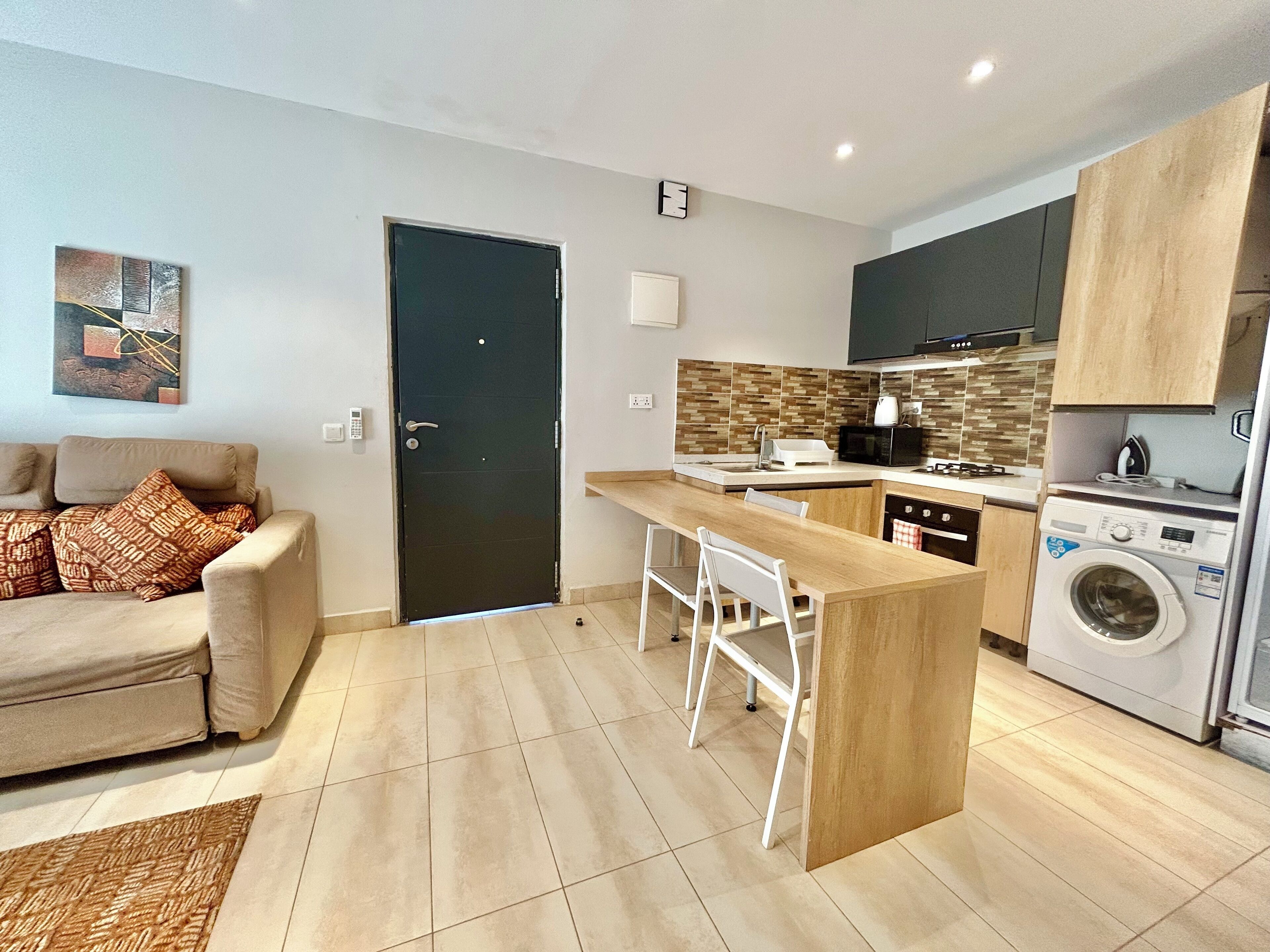 A modern kitchen with a built-in island, a washing machine, and a dining area with a sofa and chairs.