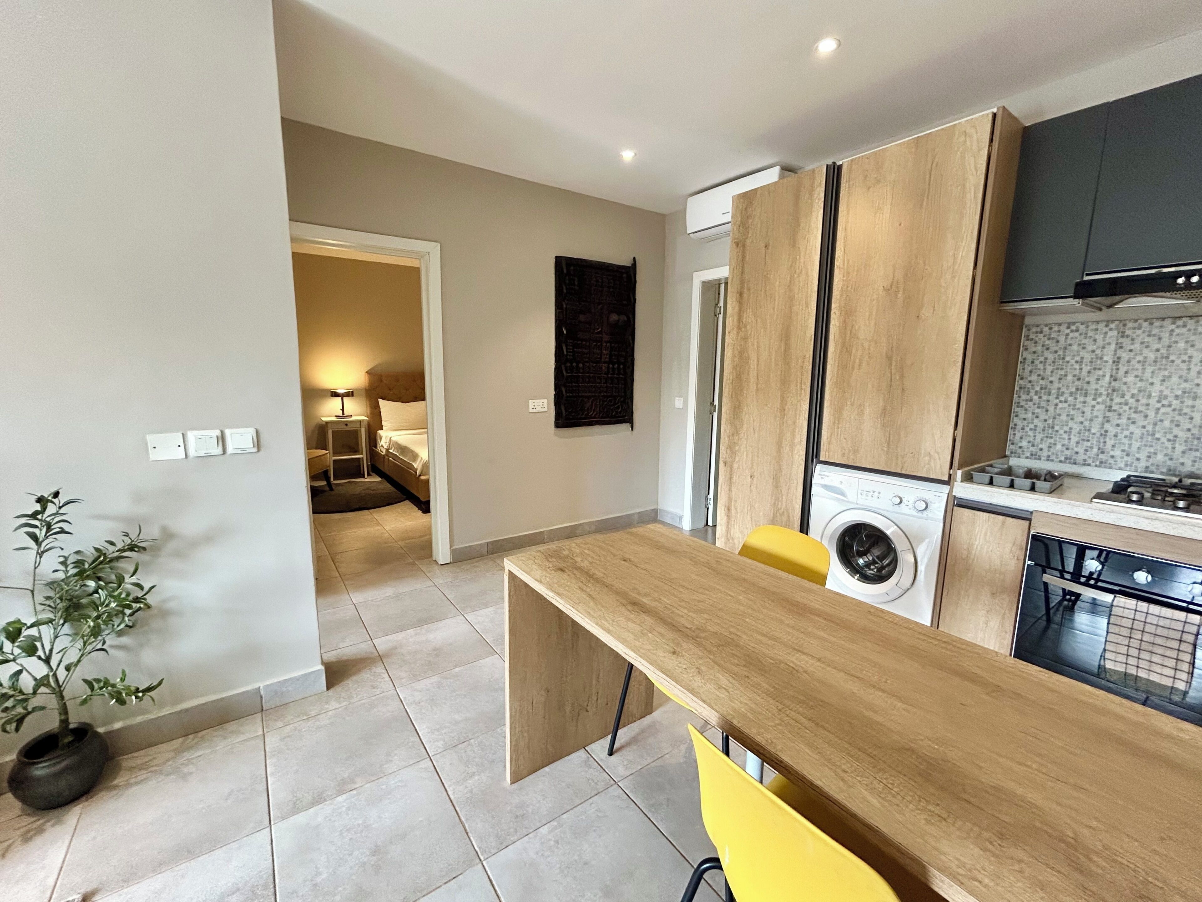 A modern kitchen with a wooden countertop, a washing machine, and a dining area with yellow chairs.