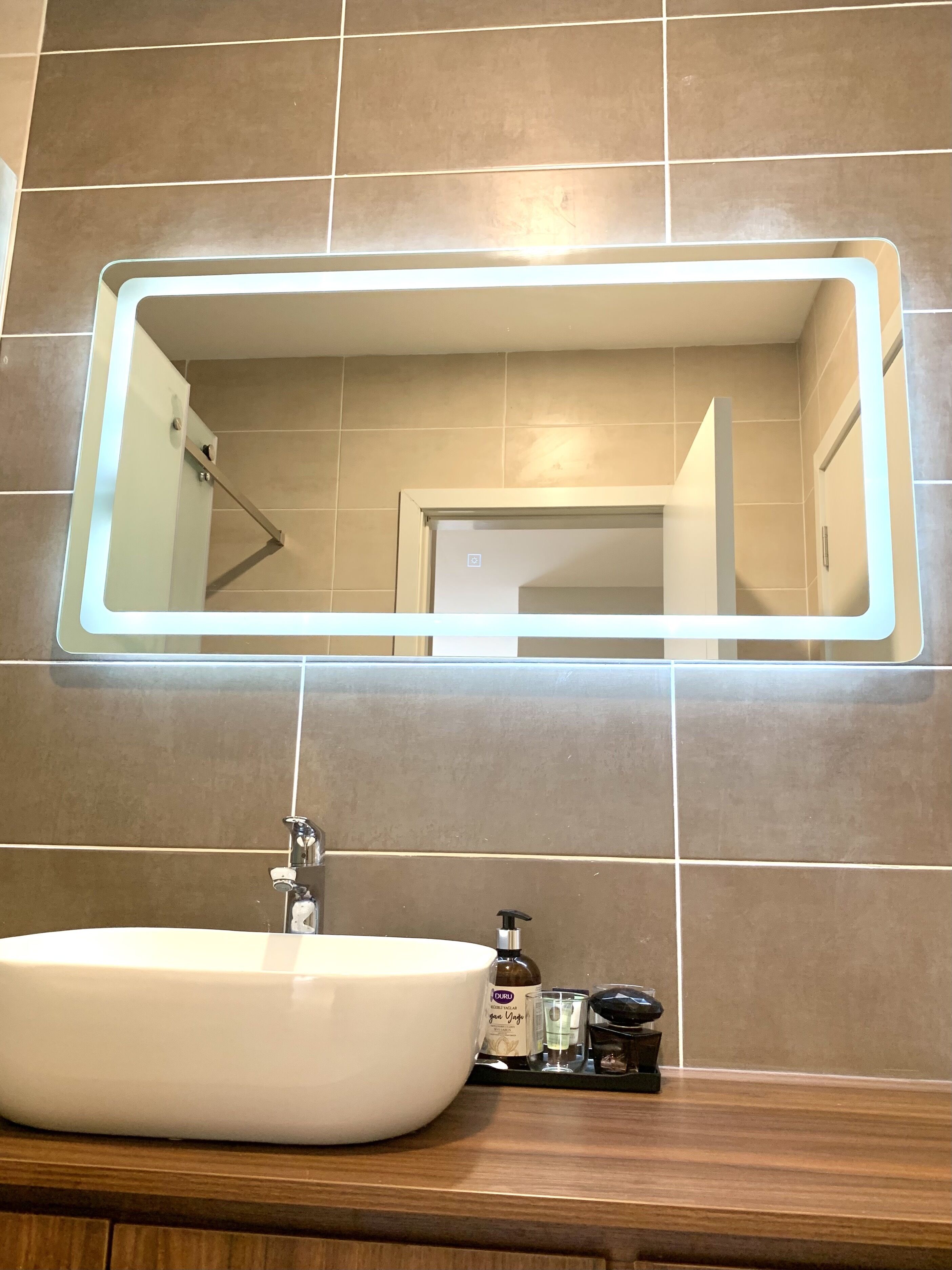 Ein Badezimmer mit einem großen Spiegel, einem weißen Waschbecken und einer sichtbaren Dusche im Spiegelbild.