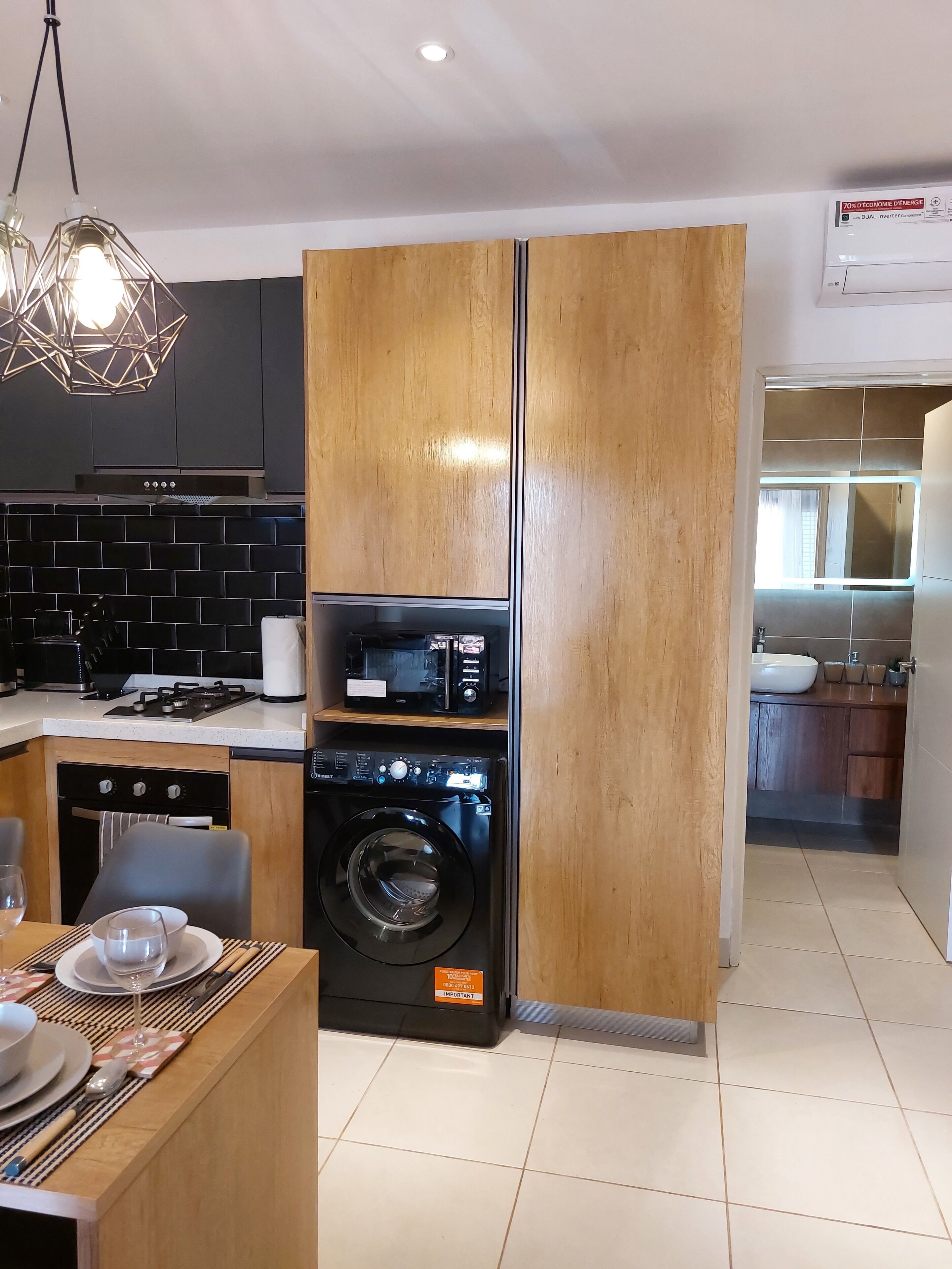 A modern kitchen with a built-in washer and dryer, a dining area with a table set for two, and a view into the adjacent bathroom.