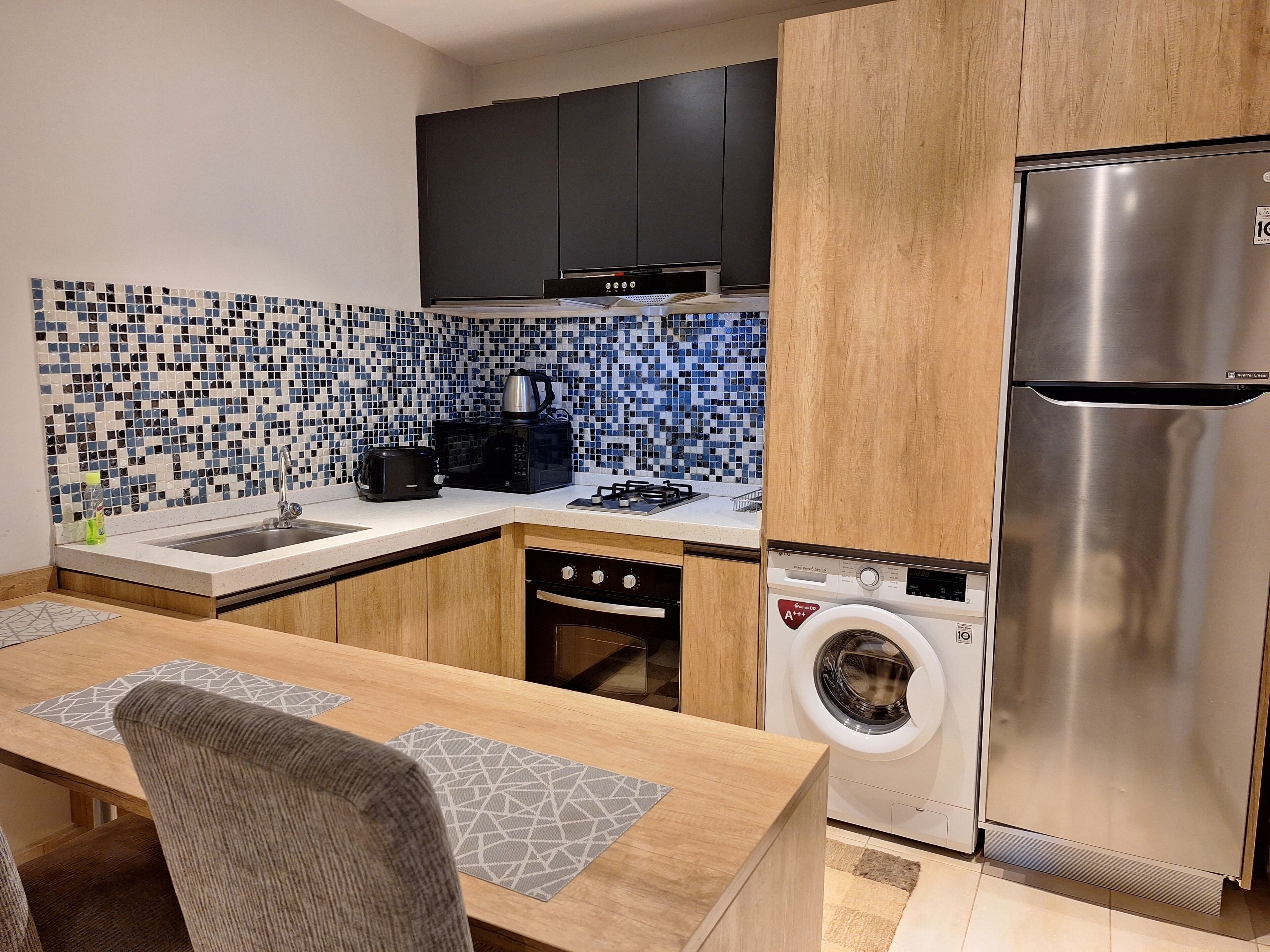 Cocina compacta con lavadora, refrigerador de acero inoxidable, microondas y tostadora.