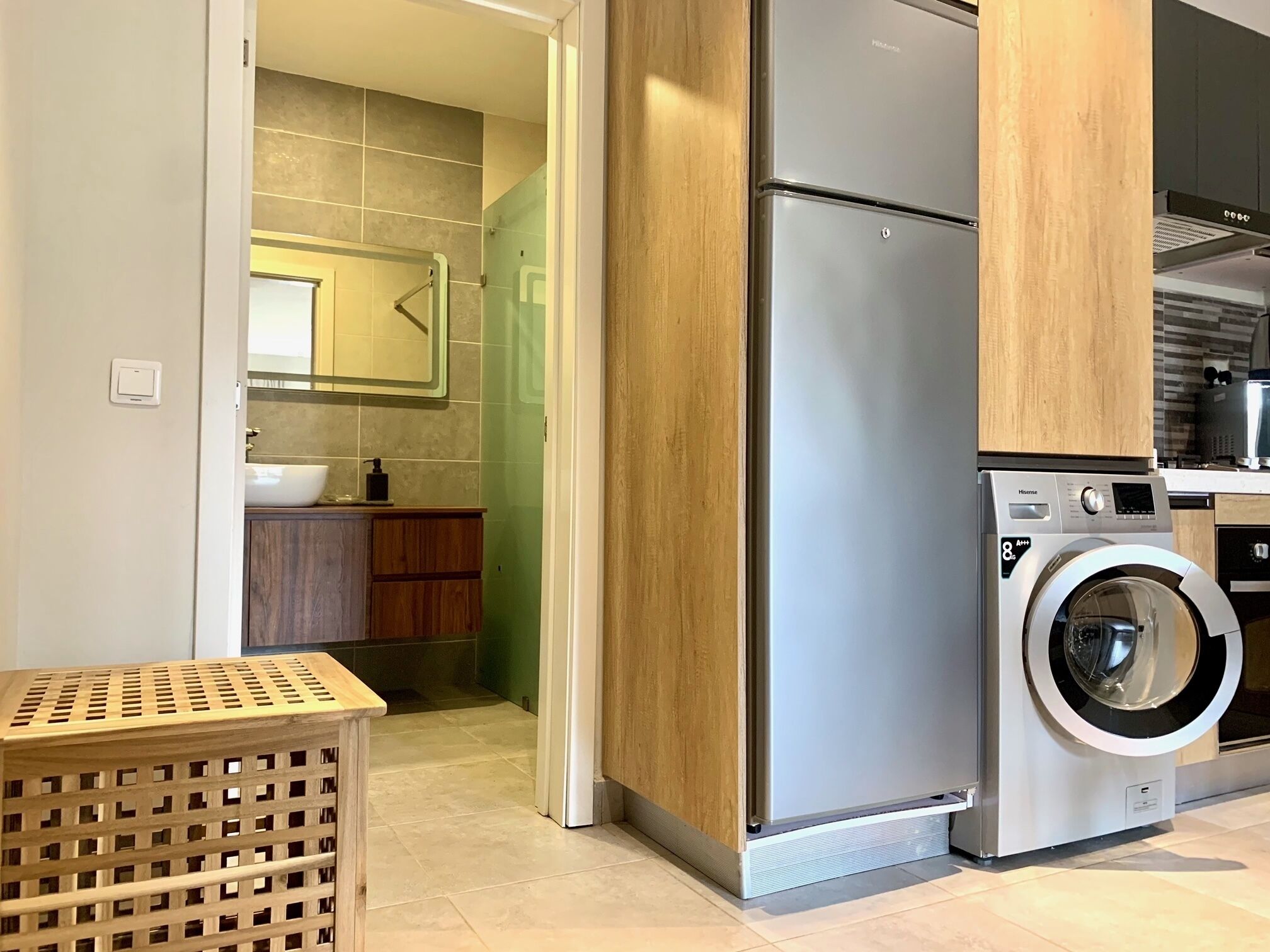 Een moderne keuken met een koelkast van roestvrij staal, een wasmachine, houten keukenkastjes en een betegelde spatwand.
