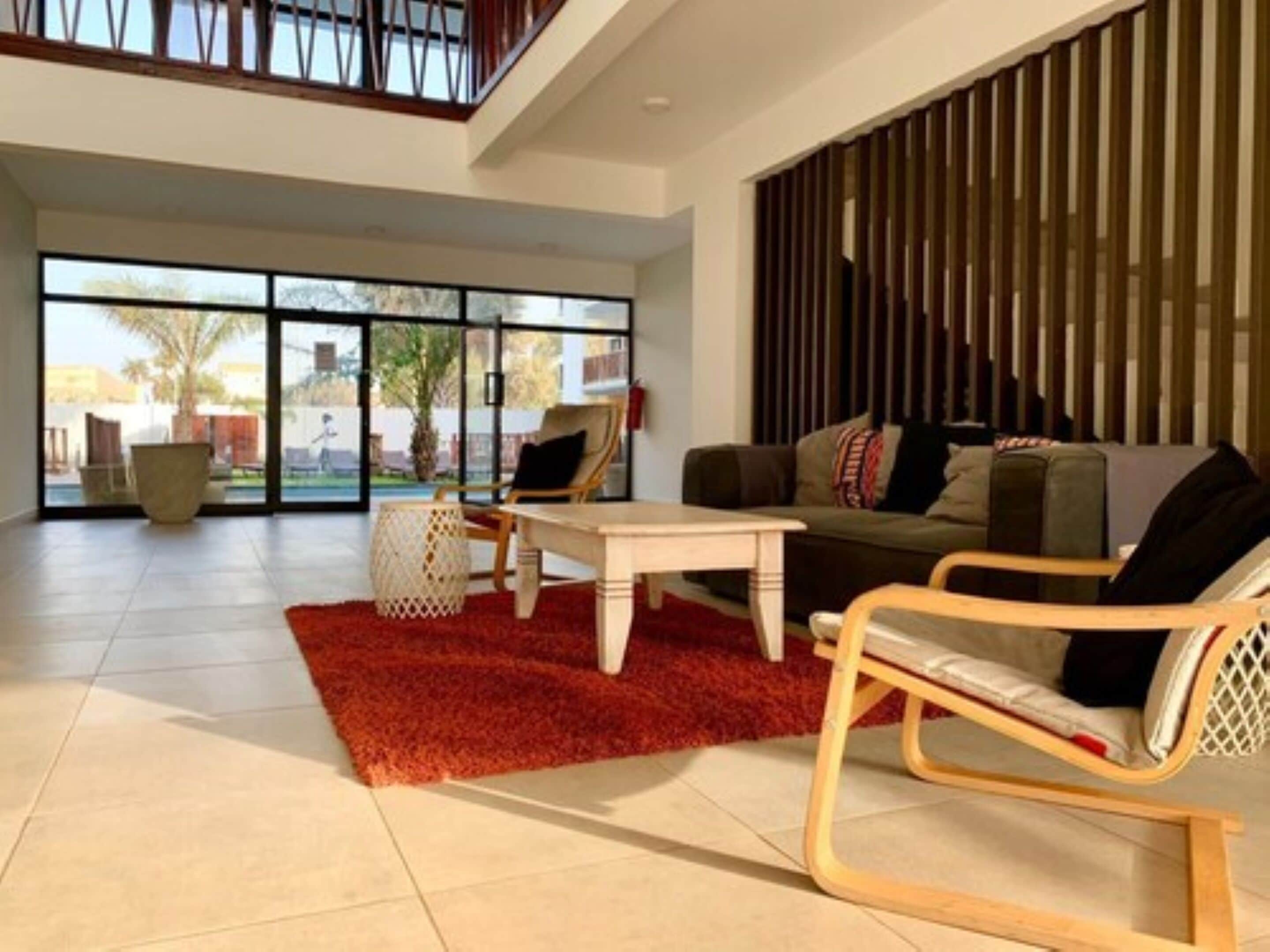 A spacious living area with a large window, a wooden coffee table, a sofa, and a red rug.