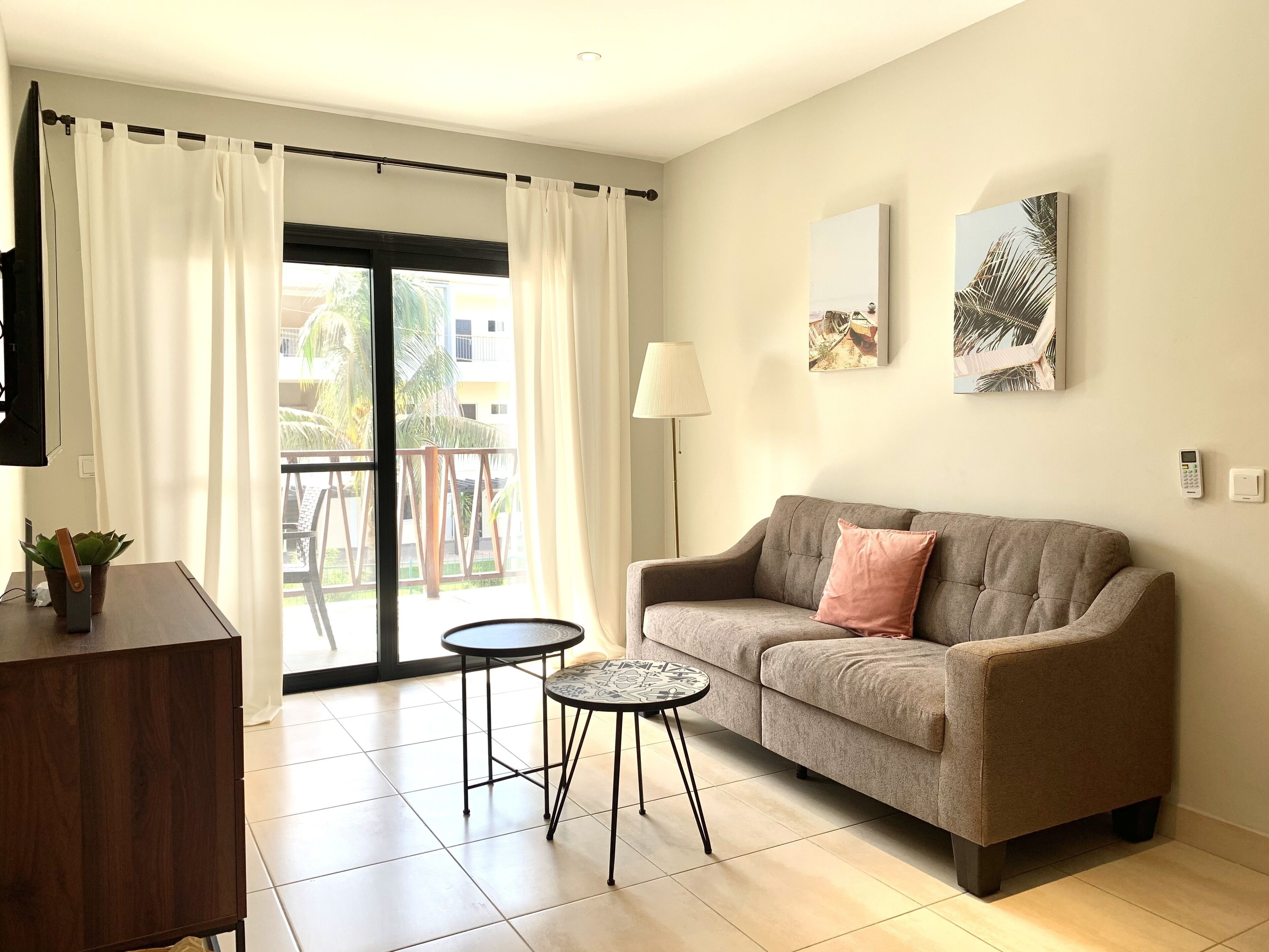 Un salon avec un canapé, deux petites tables, un téléviseur et un balcon agrémenté de rideaux.