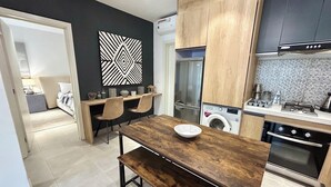 A modern kitchen with a wooden table, two chairs, a washing machine, and a stove. - Forest View Apartments (Serrekunda)