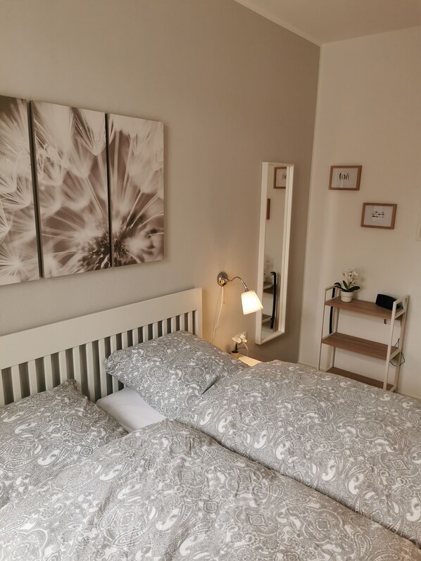 A bedroom with a bed, a nightstand, a mirror, and wall art.