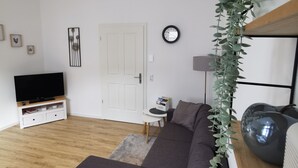 A modern living room with a grey sectional sofa, a flat-screen TV on a white entertainment unit, a small side table, and a potted plant. - Vacation apartment Ahr-Flair (Bad Neuenahr-Ahrweiler)