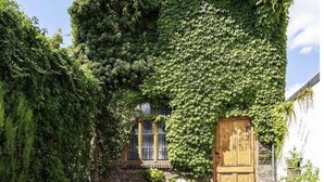 A stone patio with a round table and two striped chairs, surrounded by potted plants and a stone wall. - Vacation apartment Ahr-Flair (Bad Neuenahr-Ahrweiler)
