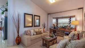 A living room with a sofa, a coffee table, and a TV stand. There is a window with curtains and a lamp on the side. - NEW LISTING Stunning Villa - Amazing Value - Lake Berkley (Kissimmee)