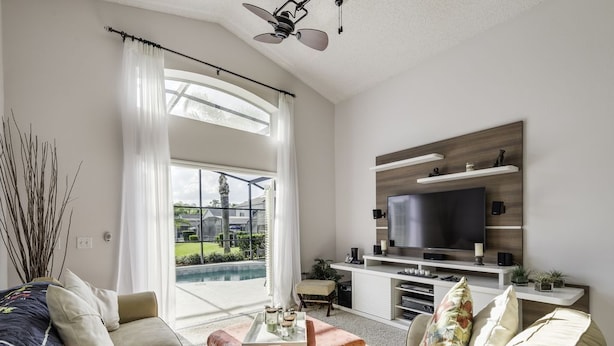 A modern living room with a large flat-screen TV, comfortable seating, and a view of a pool. - NEW LISTING Stunning Villa - Amazing Value - Lake Berkley (Kissimmee)