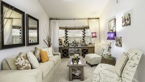A living room with a sofa, armchair, coffee table, and a bookshelf filled with books and decorative items. - NEW LISTING Stunning Villa - Amazing Value - Lake Berkley (Kissimmee)