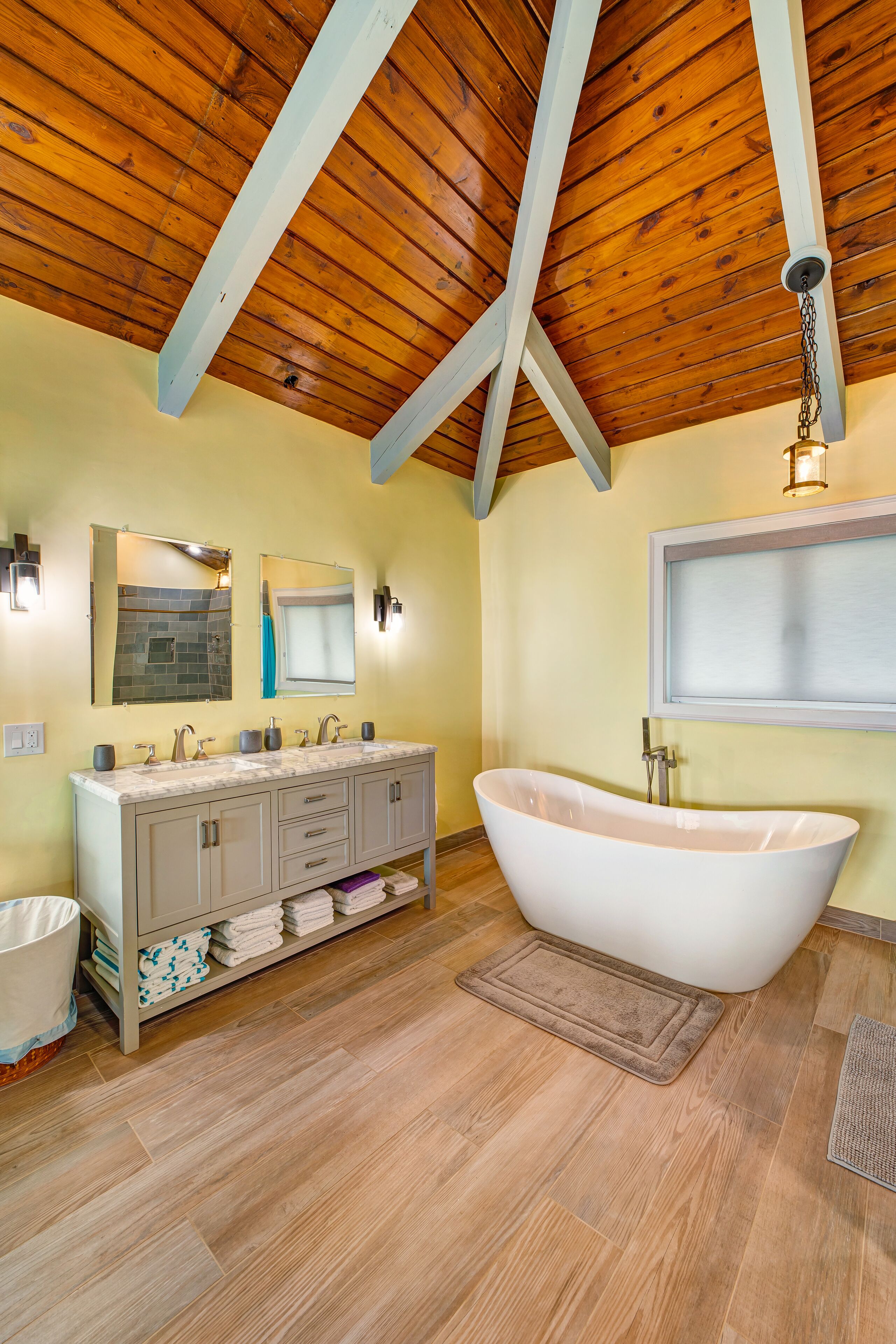 A bathroom with a freestanding bathtub, a vanity with a mirror, and wooden beams on the ceiling.