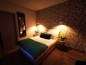 A bedroom with a bed, green throw, two bedside tables with lamps, a mirror, and a patterned wall. - Casa do Castelo (Sernancelhe)